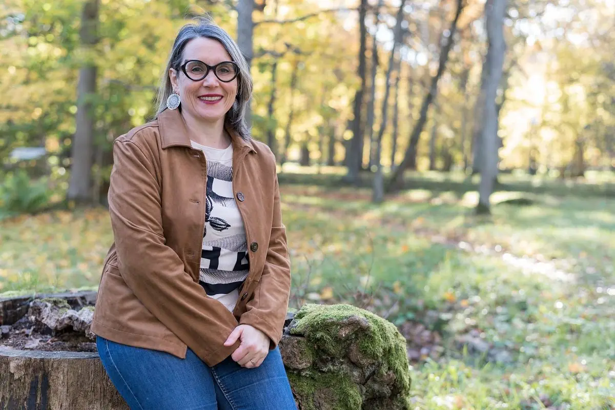 Communication animale : Sophie Bordes-Meunier assise sur une souche couverte de mousse, dans un parc en automne