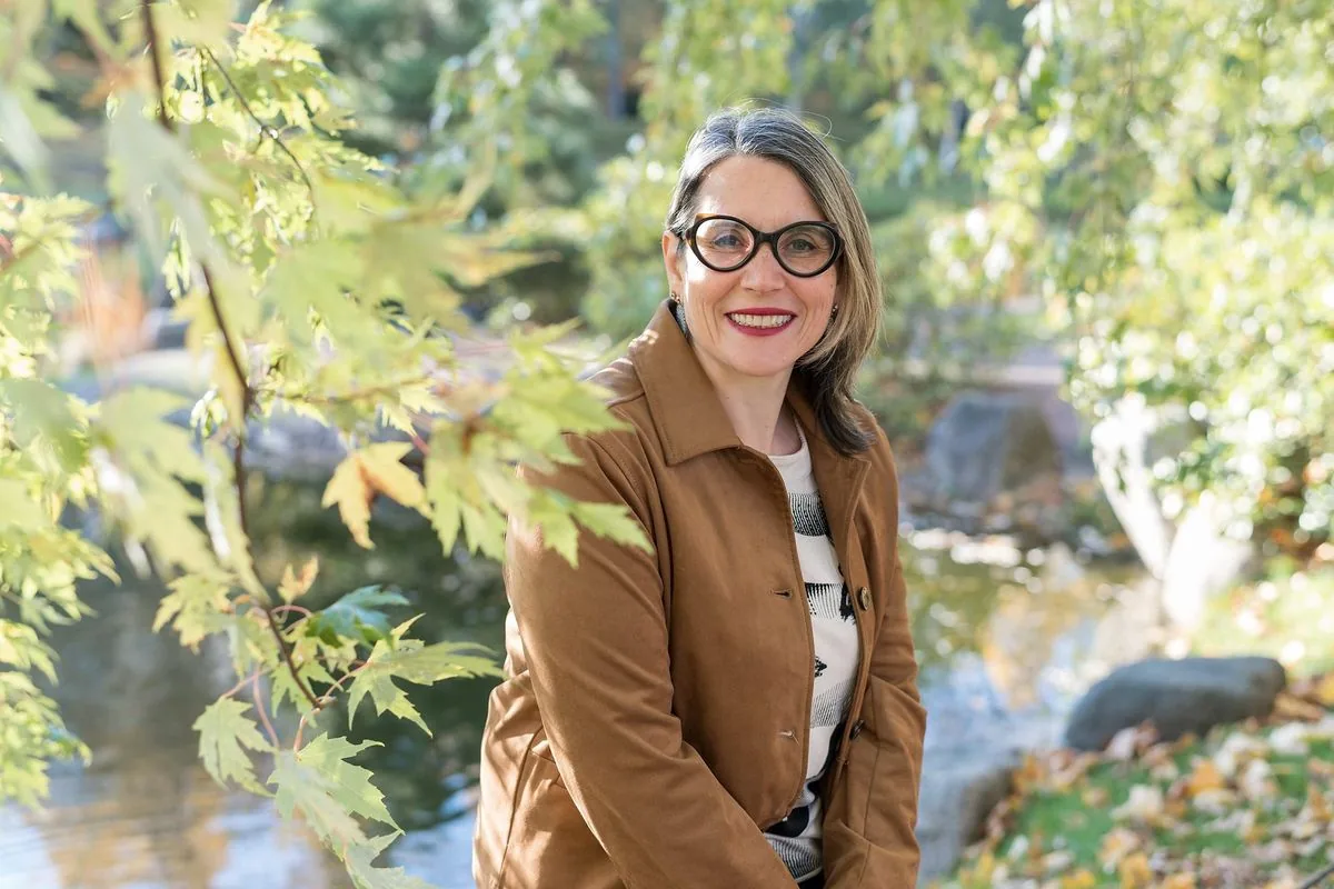 Communicatrice animalière : Sophie Bordes-Meunier sourit, assise au bord d’un étang dans un jardin d’automne