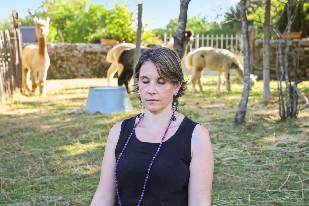 Formation soins énergétiques pour animaux : Sophie, les yeux fermés, dans un pré où paissent des alpagas
