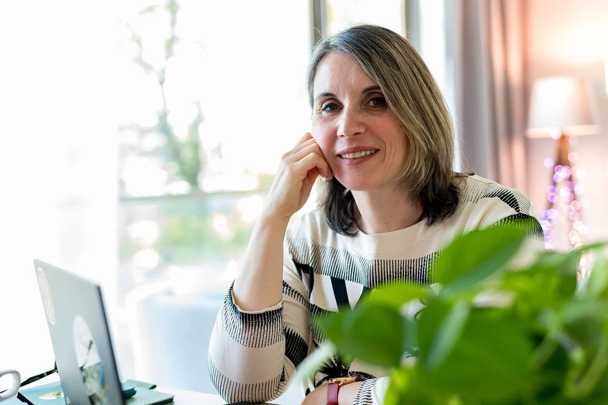 Formations en ligne : Sophie sourit, la joue dans la main, assise à son bureau