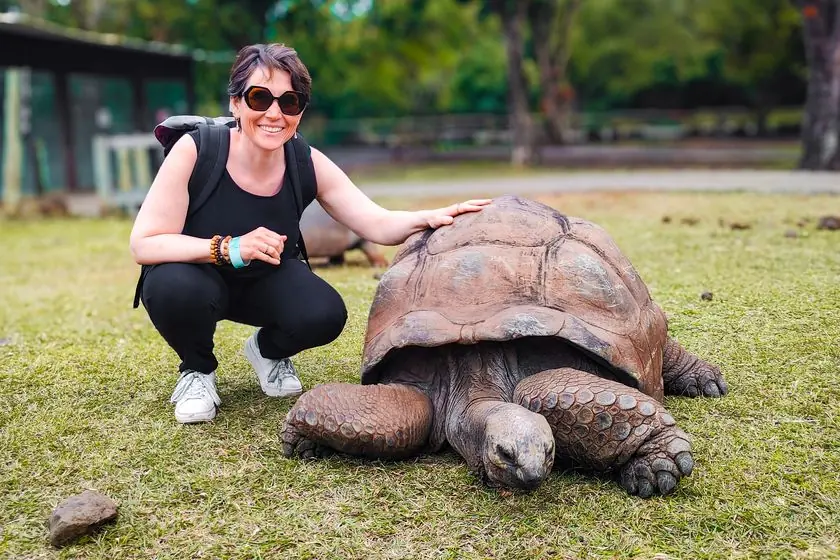 Formations en ligne : Sophie accroupie dans l’herbe, la main posée sur la carapace d’une tortue géante