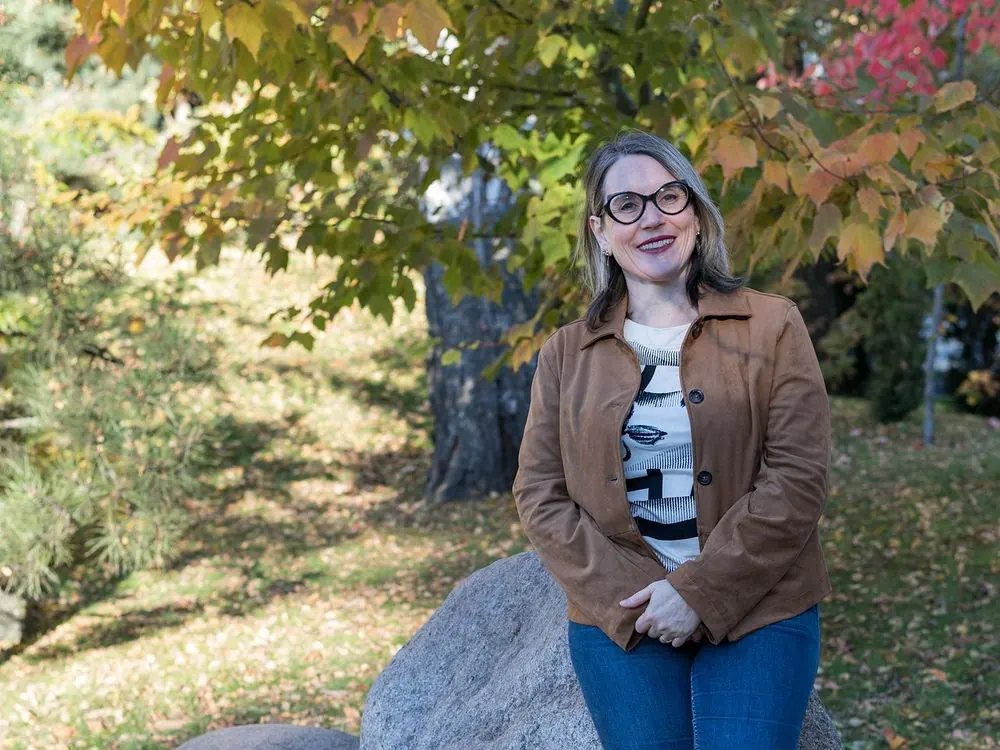 Méditation de groupe en ligne : Sophie Bordes-Meunier debout près d’un rocher, sous un érable en automne