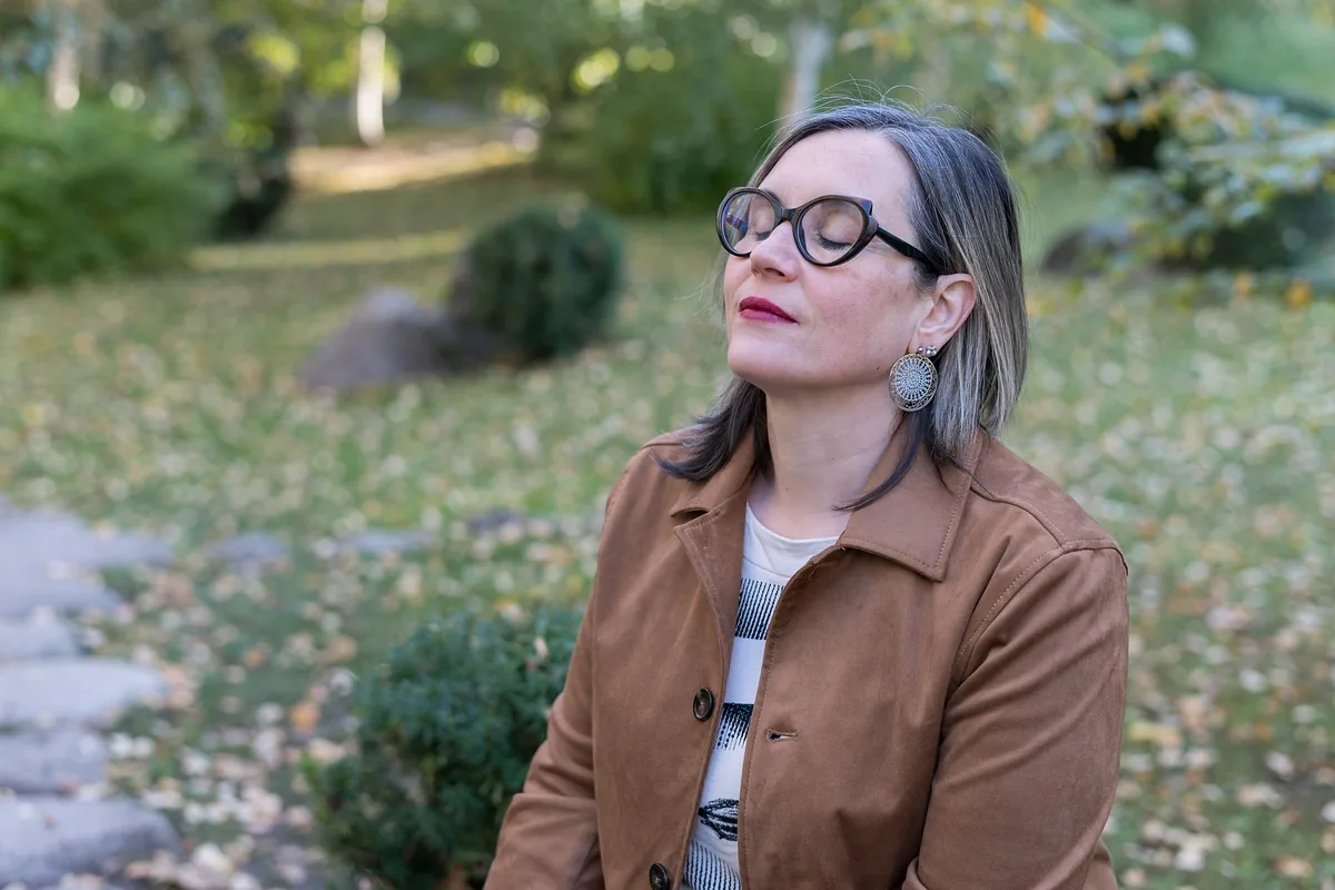 Soin énergétique à distance : Sophie, les yeux fermés, savoure un moment de calme dans un jardin d’automne
