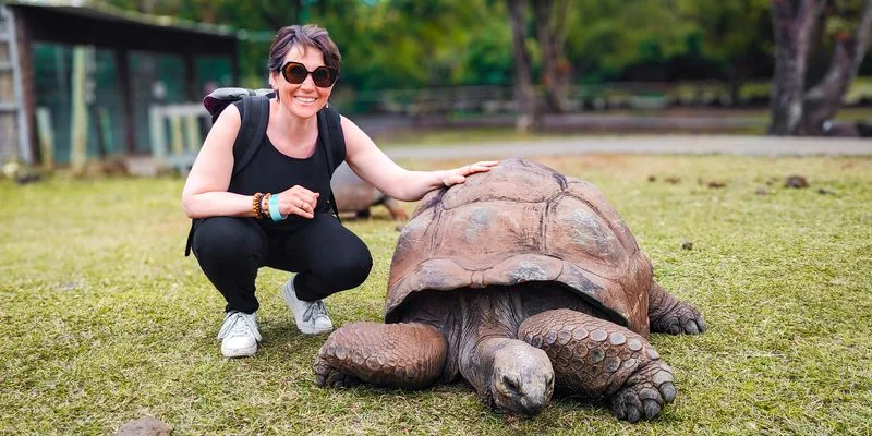 Tarif communication animale : Sophie accroupie dans l’herbe, la main posée sur la carapace d’une tortue géante
